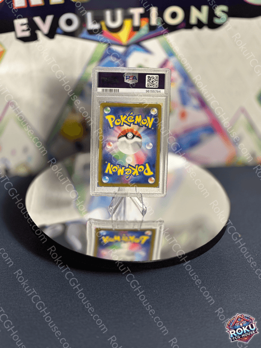 Graded Pokémon card displayed on a mirror surface, featuring colorful artwork of the iconic Poké Ball.